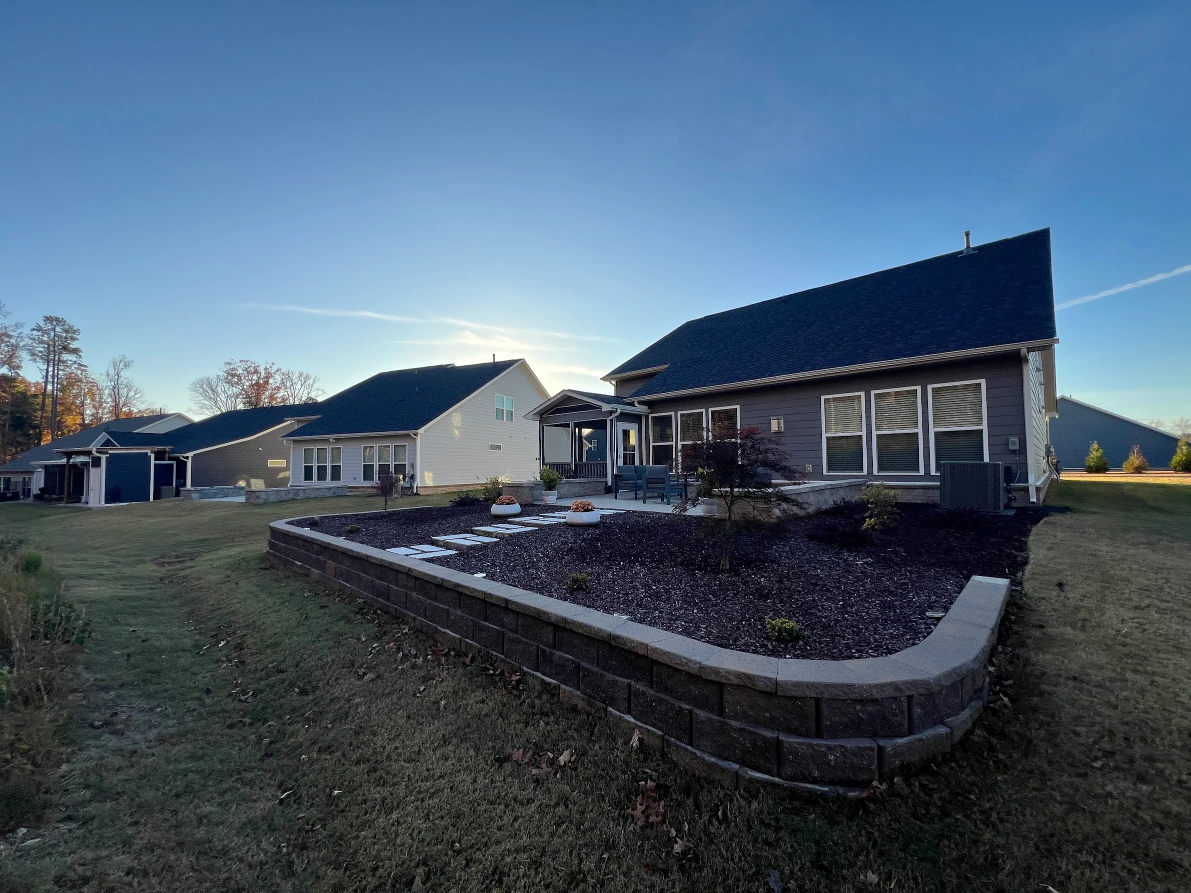 Stone retaining wall with dark mulch landscape bed and concrete edging behind residential home