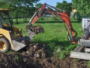 Compact track excavator removing soil during landscape site preparation