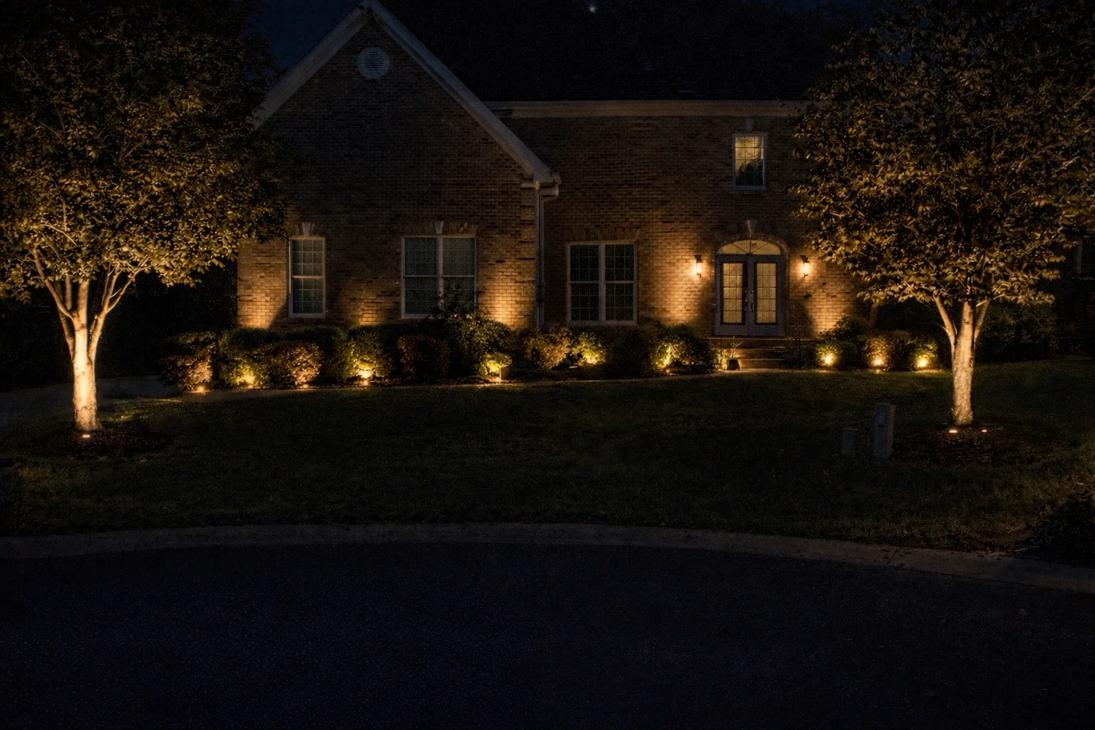 Brick home with uplighting on trees, foundation plantings, and architectural accent lighting at night