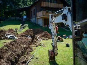 Compact excavator grading yard with fresh soil trenches and prepared landscape bed