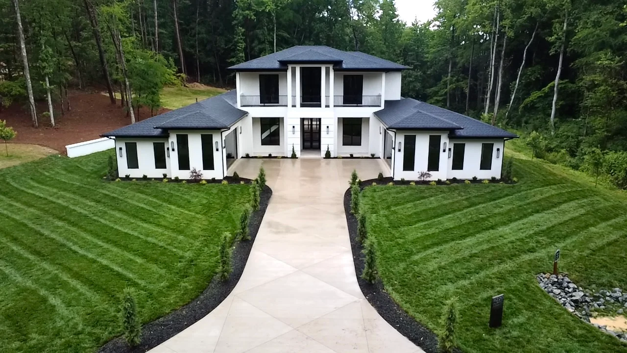 Modern white home with manicured lawn, curved concrete driveway, hedges, and dark mulch borders